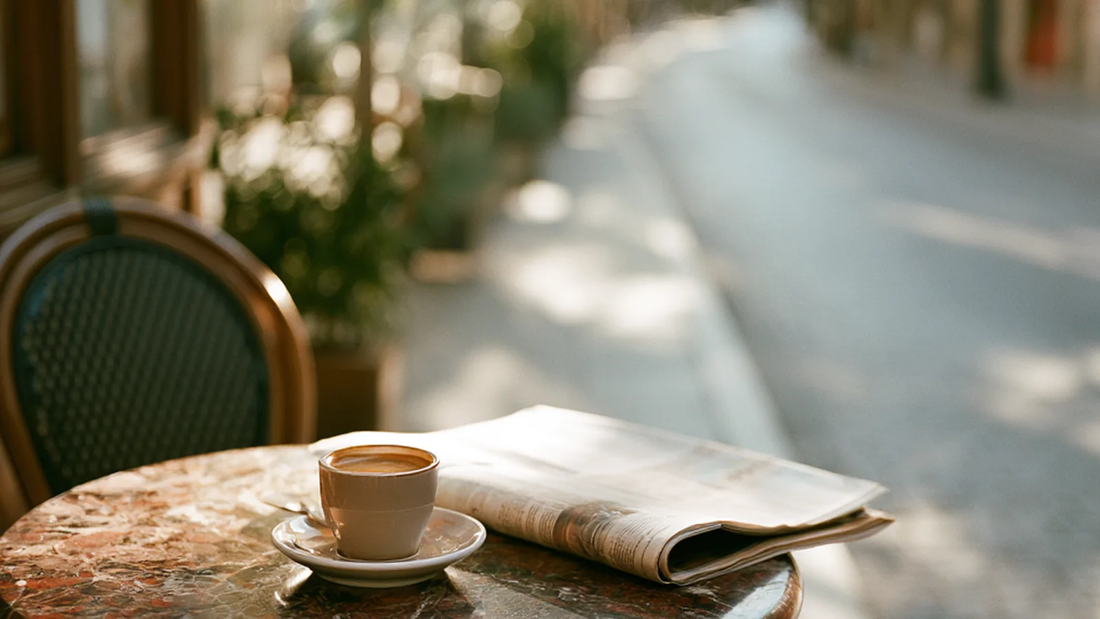 Cafe table with coffee and a folded newspaper on a quiet street